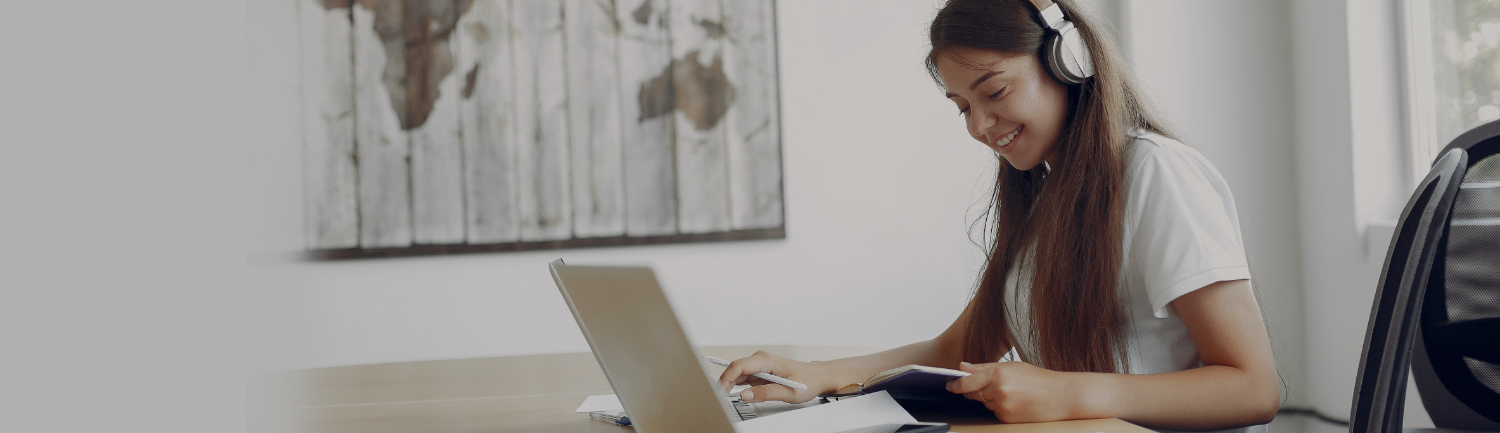 Smiling woman wearing headphones and working on a laptop at a desk, representing friendly customer support and easy communication