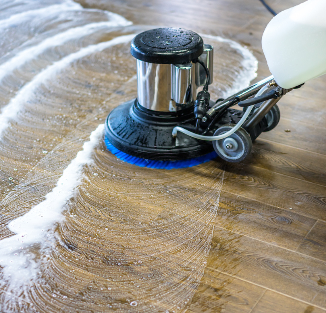 Hardwood cleaning in progress using a floor scrubbing machine to remove dirt buildup and restore the natural shine of wood flooring