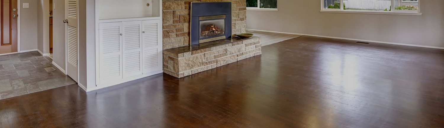 Spacious living room with smooth, polished hardwood floors and a stone fireplace, showcasing a bright home after hardwood cleaning