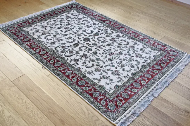 Elegant patterned area rug with detailed borders and fringe, lying flat on a wooden floor after area rug cleaning