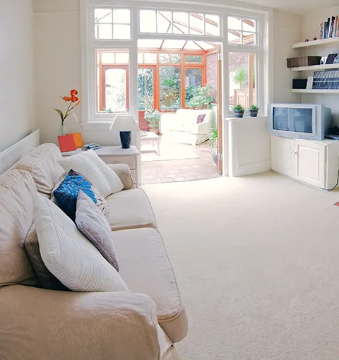 Bright and cozy living room filled with natural light, showcasing a clean, inviting home after hardwood cleaning, with soft seating, built-in shelves, and open doors to a sunlit patio