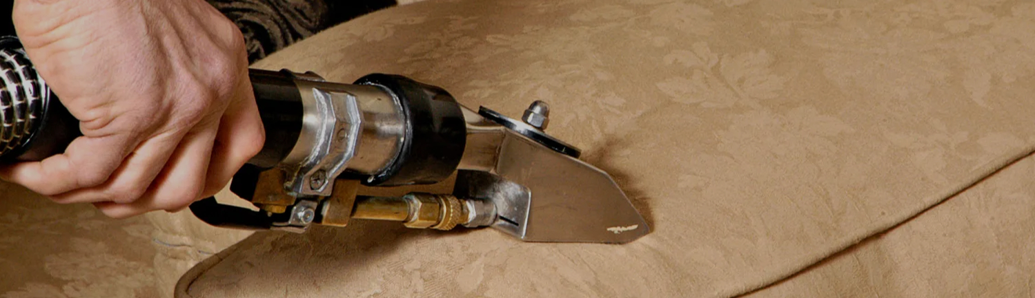 Professional upholstery cleaning in progress using a hot water extraction tool on a fabric sofa cushion, removing embedded dirt, stains, and allergens from upholstered furniture